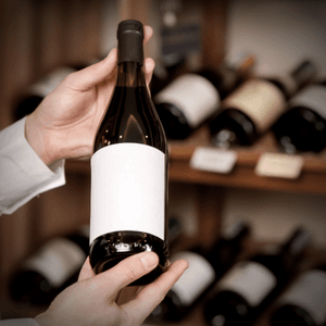 Mãos escolhendo uma garrafa entre prateleiras de vinhos